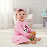 Baby in a pink outfit playing with blocks in a room with a white couch and toys.